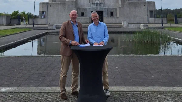 Johan Maas en Mark Vermeer staan glimlachend achter een statafel voor het gebouw van Radio Kootwijk, na het tekenen van de intentieverklaring MijnOverheid Zakelijk.